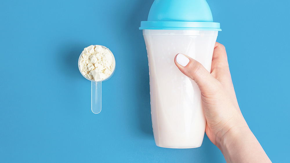 Female hands hold bottle of protein shake and a measuring spoon with protein powder